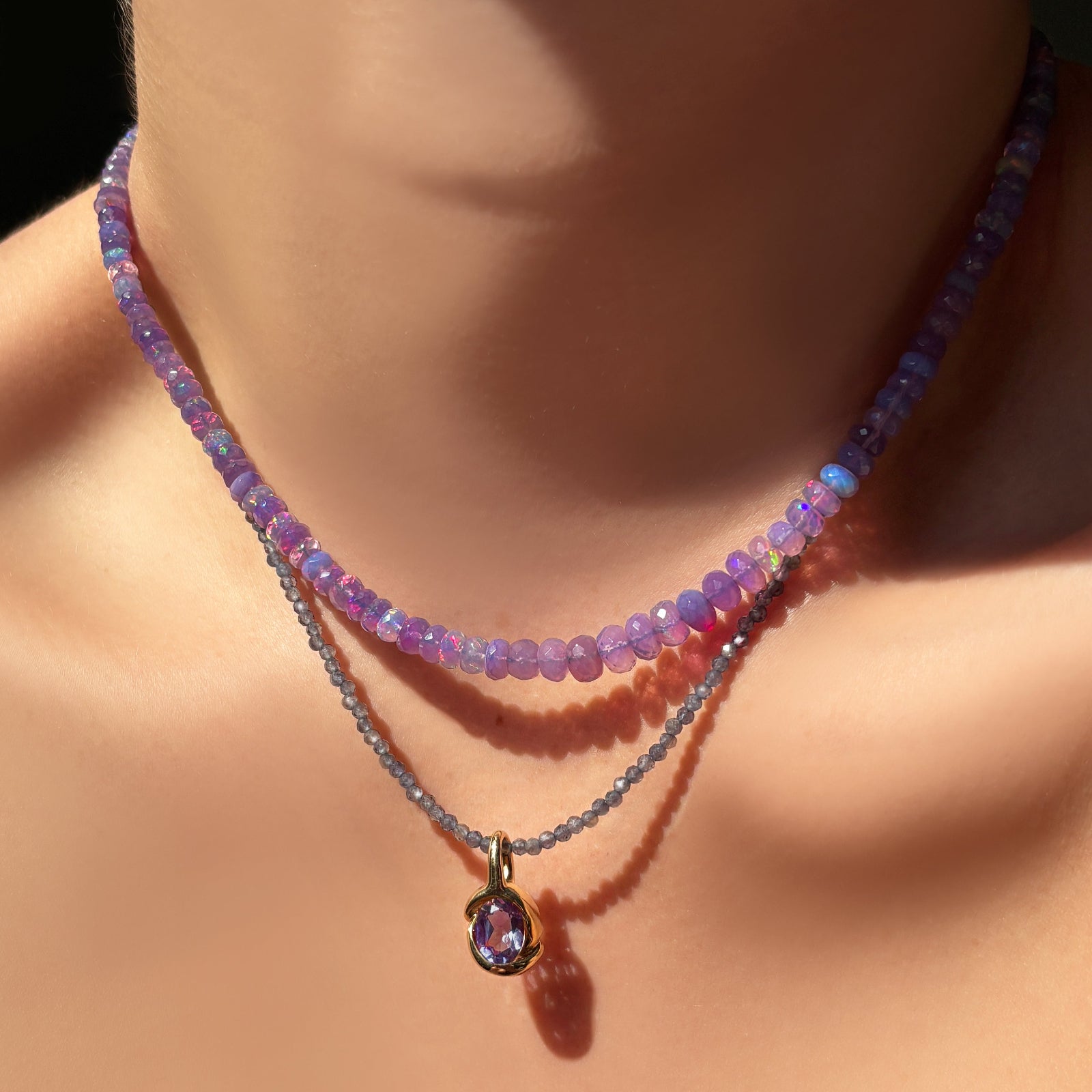 Purple beaded Necklace with a 14K recycled yellow gold amethyst molten knot charm pendant on a model's neck against a dark background.